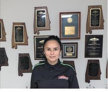 Photo of brunette female employee in front of a wall with awards hanging