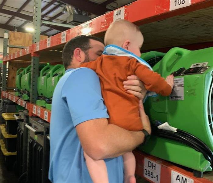 Photo of Cates Culpepper holding his son, Kip, in front of green equipment in warehouse.
